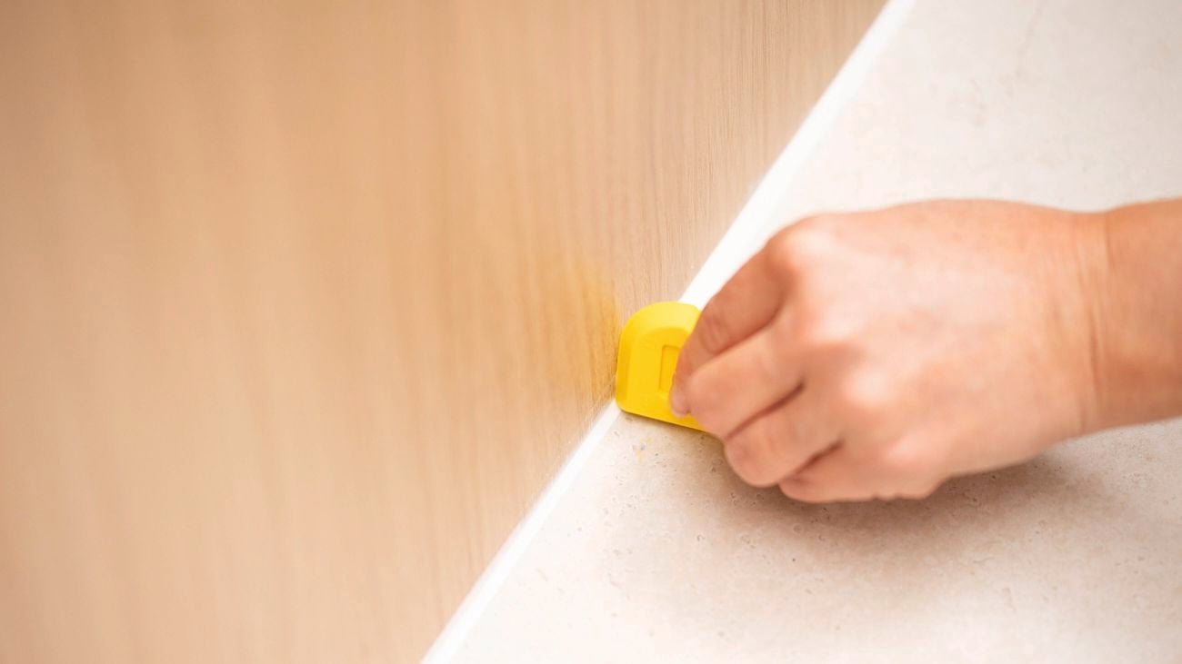 A person is using a caulking tool to smooth freshly applied bead of silicone sealant.