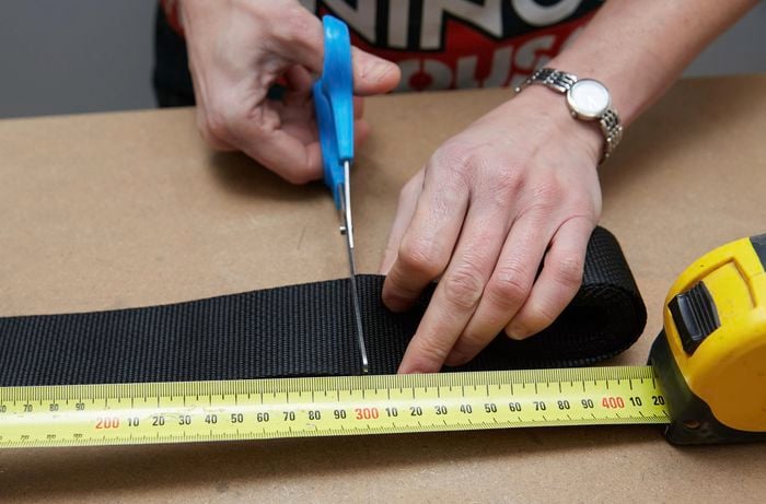 A person cutting a length of webbing with scissors, using a measuring tape