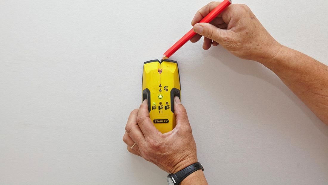 Using a stud finder to find and mark the wall studs.