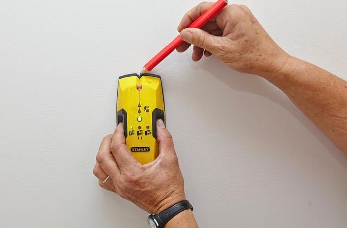 Using a stud finder to find and mark the wall studs.