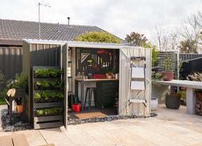 Dark shed in garden with doors open to show interior pegboard with tools attached and wooden desk