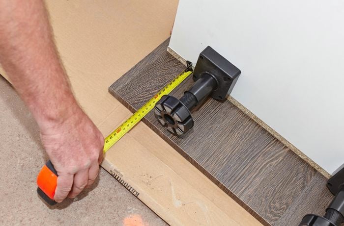 A person measuring the height of adjustable legs with a measuring tape