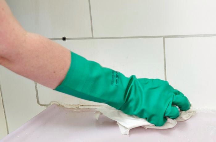 A person wearing rubber gloves wiping a long a line of grout with a rag