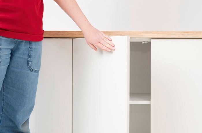 : A person is softly closing a cabinet door with a newly installed hinge plate to check its alignment. 