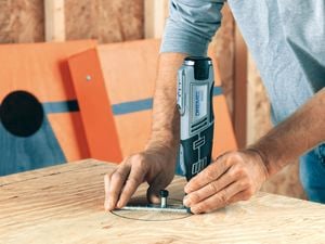 Person using a Dremel tool to cut a hole in plywood.