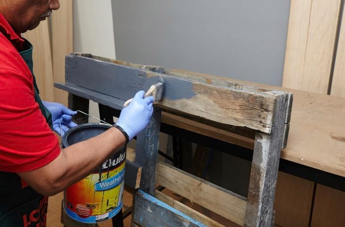 A person painting a shelving unit made of recycled timber