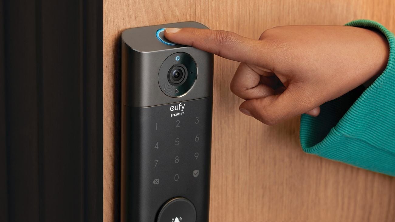 Eufy Security video smart lock installed on a wooden door, with a finger pressing the fingerprint detector