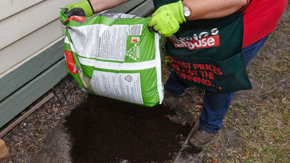 A person emptying a bag of compost into a garden bed