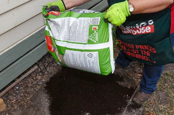 A person emptying a bag of compost into a garden bed