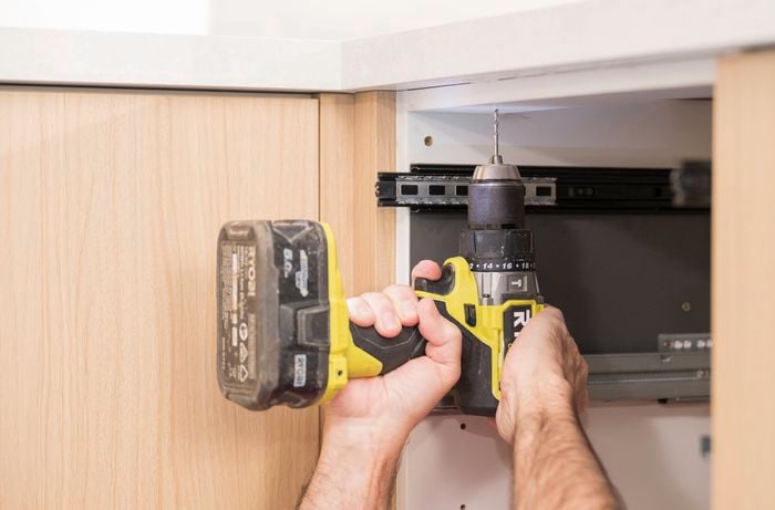  A person uses a drill to pre-drilling pilot holes through the cabinet rails.