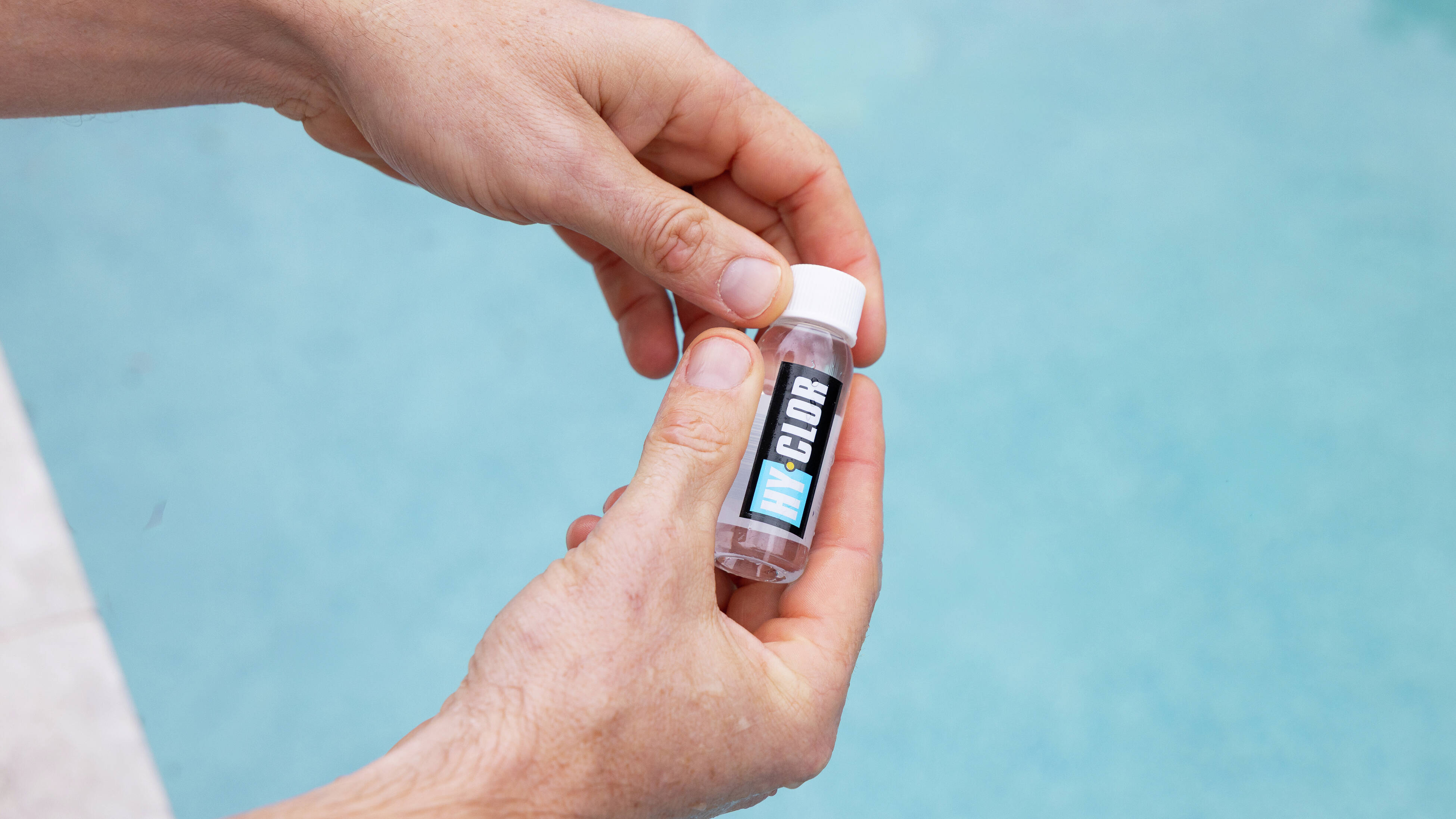  Hands holding a small pool water testing vial labeled “Clor.”