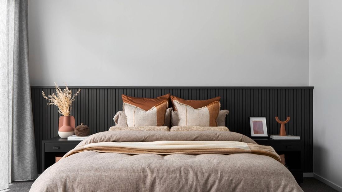 Modern bedroom with panelled walls, bedside tables and bed with earth coloured bedding, cushions and throw.
