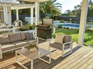 Contemporary deck with outdoor lounge furniture, a dining setup under string lights, a barbie cooking food, and a garden with a pool.