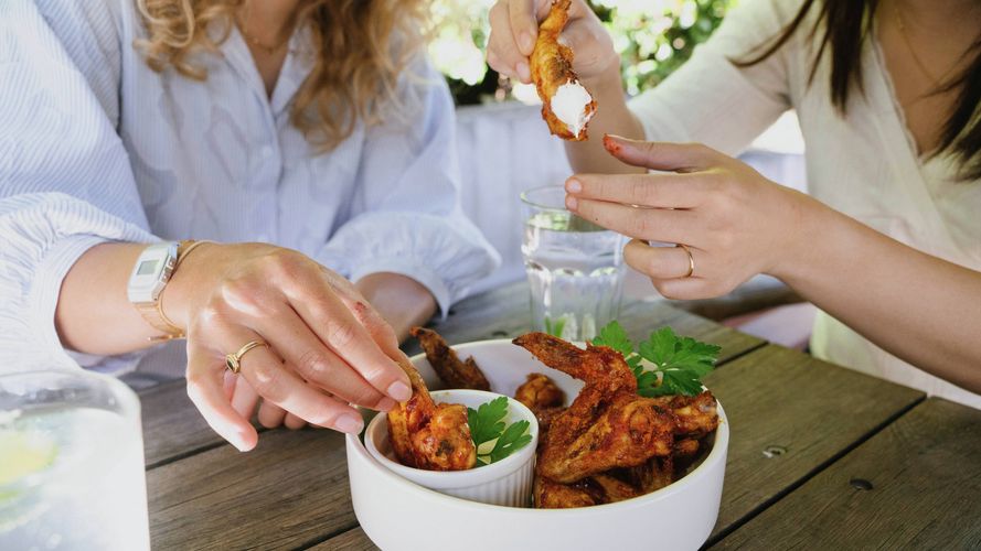 Two people sharing spicy chicken wings with dipping sauce at an outdoor table.