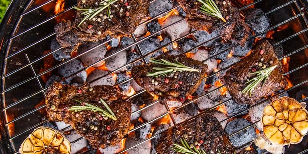 Close up of various cuts of seasoned meat cooking on a coal fired kettle barbecue