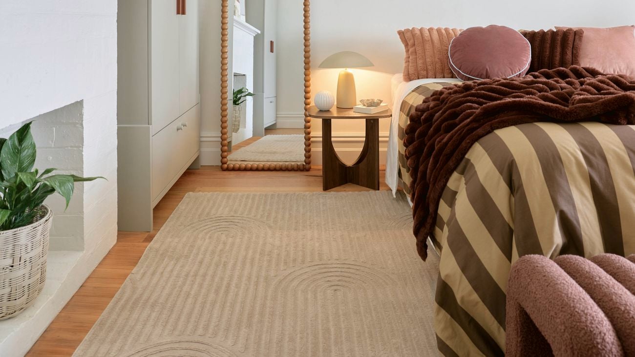Living room featuring a sofa, patterned area rug, coffee table and cushions styled in warm neutral tones.