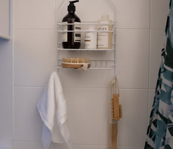 A small plastic hanger for shower products. Stored inside is Aesop soap, Olaplex hair treatments and hanging from the bottom hooks are a face washer and exfoliating brush.
