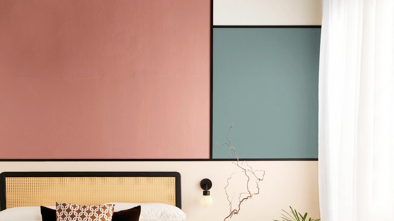 A modern bedroom interior with a cane‑headboard; colour‑blocked walls in pink and green with black trim.