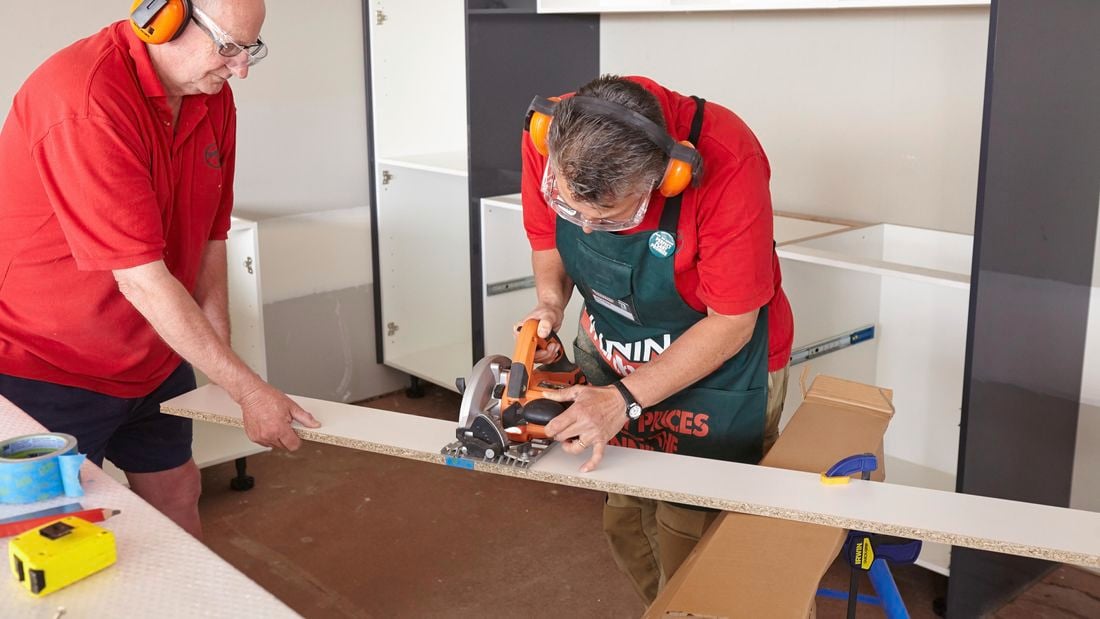 One person cutting a length of kickboard with a circular saw while another person holds the end
