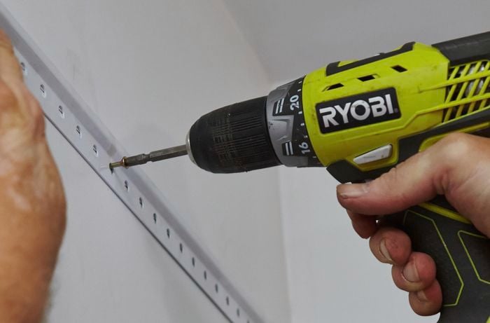 Horizontal tracks for shelving being screwed into the wall of a walk in wardrobe with a power drill