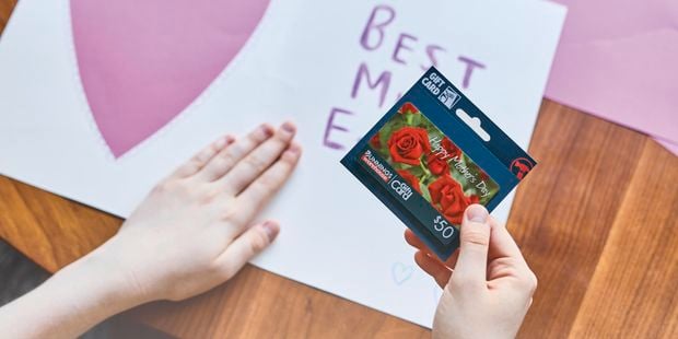Person holding gift card with Mother's Day card in background