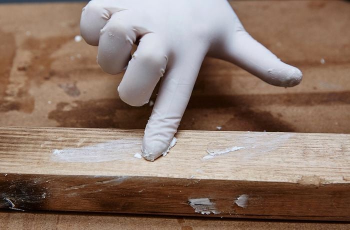 Person wearing a glove and applying spakfilla to holes in timber.