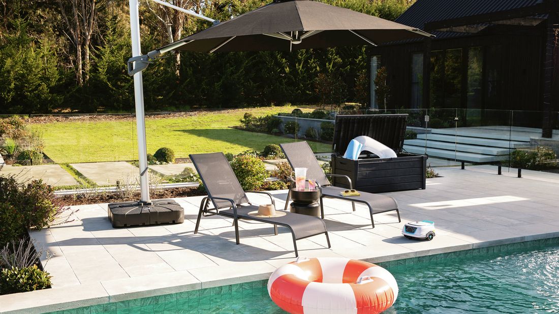 Outdoor patio with a large black umbrella, two lounge chairs, a swimming pool with an inflatable ring, and a garden.