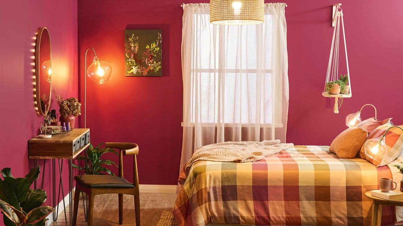 A bedroom with walls painted in Dulux Ripe Rhubarb, a checked quilt cover and a hanging plant