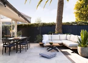 A red stained outdoor dining set on a matching red stained deck, with a pool nearby