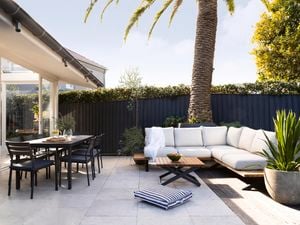 A red stained outdoor dining set on a matching red stained deck, with a pool nearby