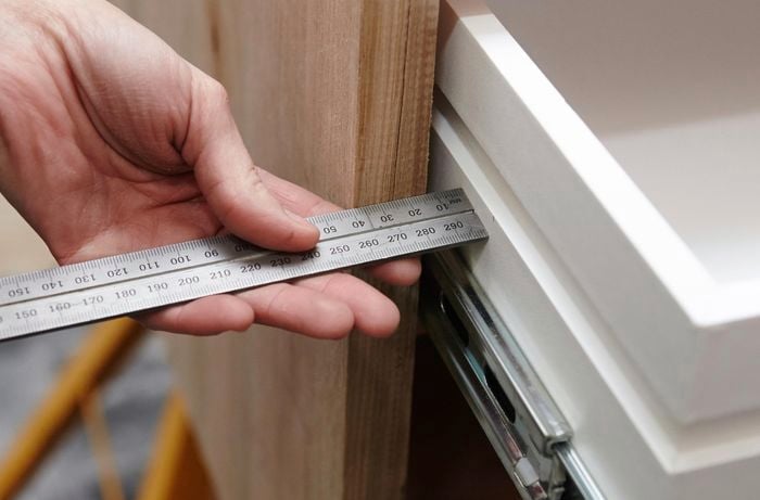 A person using a metal ruler to measure between a drawer and a timber panel