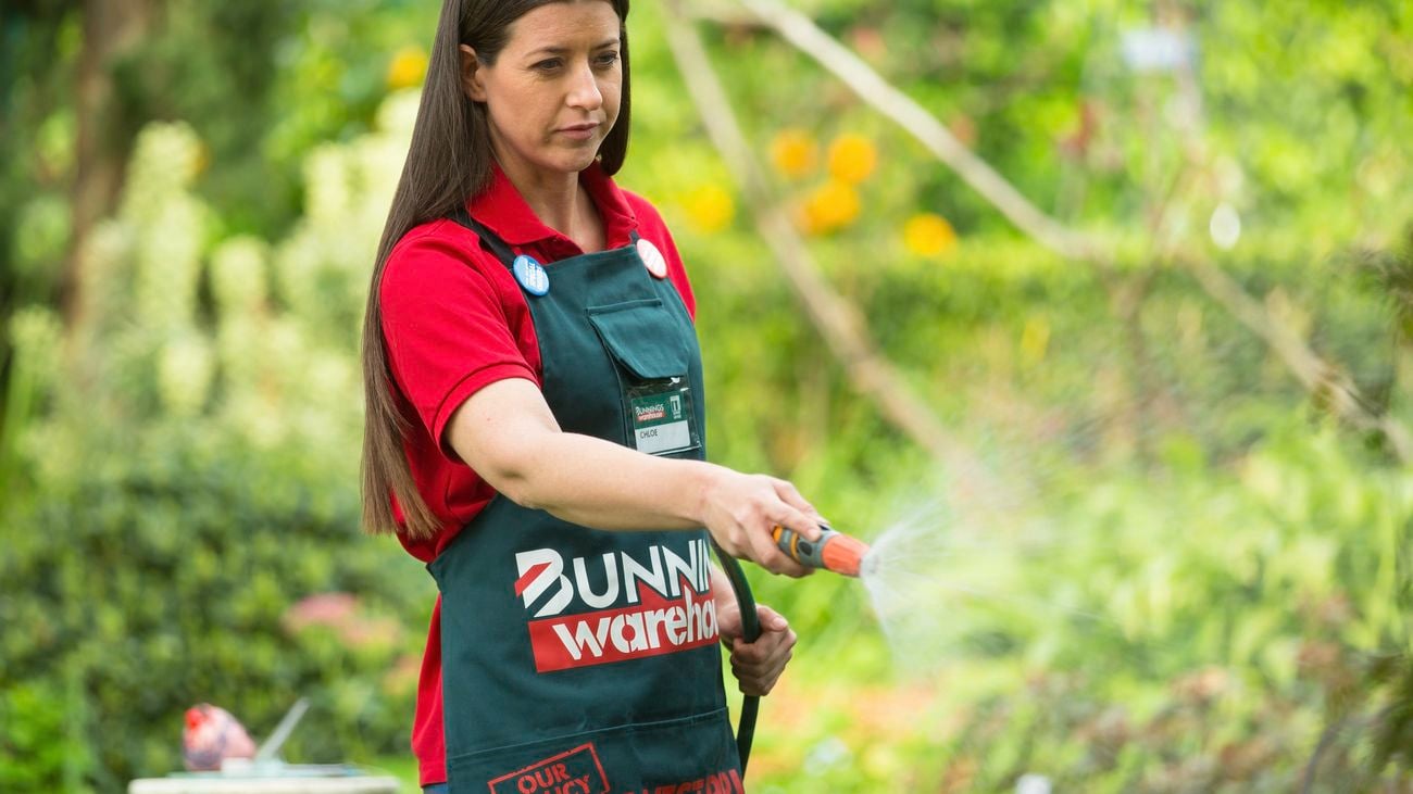 A Bunnings team member watering the garden with a hose