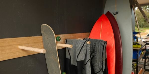 Wooden rack against a wall with a skateboard, wet suits and surfboards hanging on it