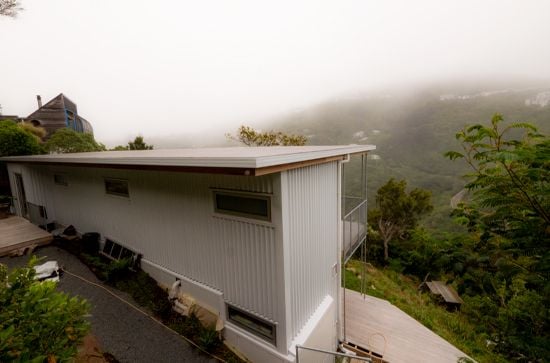Rear view of a two-story sustainable house on a hillside with misty outlook