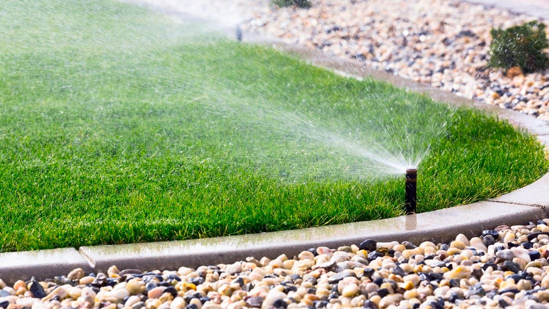 Image of sprinkler system watering grass that meets a stone garden bed