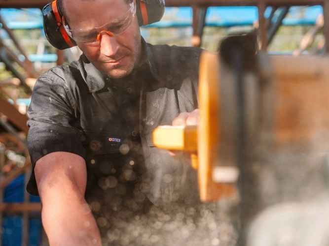 A male with ear muffs on using an electric saw on a construction site.
