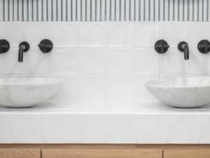 An image of a bathroom with white tiles and black tapware