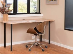 A room with a desk, chair, window, and a flower vase on the desk 