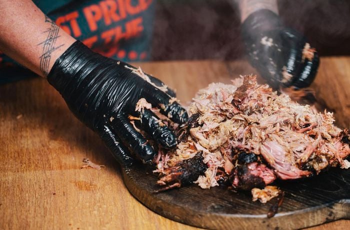 Person pulling apart smoked pork shoulder