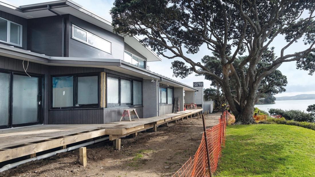 A large house with a back deck in front of a large tree overlooking a coastline
