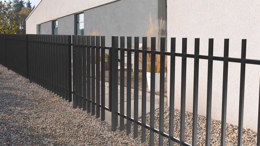 Fencing on the side of a modern house with stones and pavers.