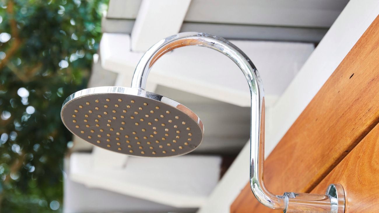Close up of stainless steel outdoor shower head against a timber splashback.