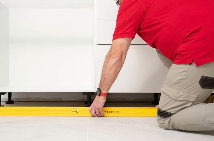 A person is using a spirit level to check that the base cabinets are evenly aligned on the floor.