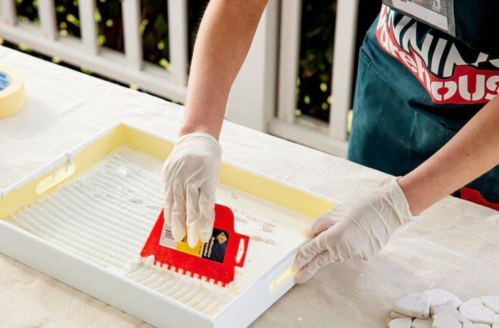 A woman applies an adhesive-and-grout mix over the surface of a tray.