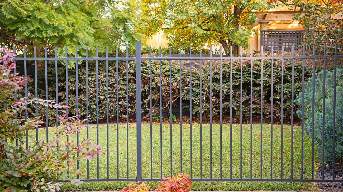 Steel-coloured backyard gate separating stone pavement and lawn.