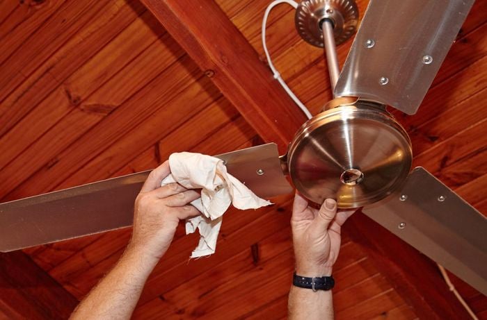 Person cleaning the blades of a ceiling fan