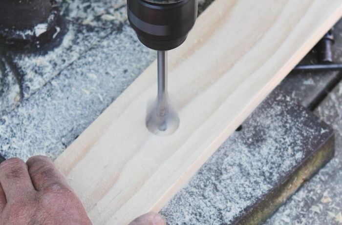 A bore spade drill bit being used to gouge a hole in a piece of timber as a base for a dowel Christmas tree