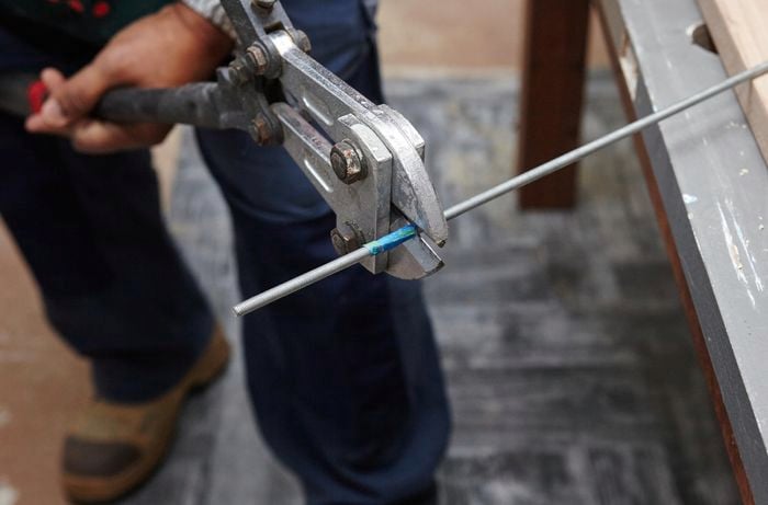 A person cutting a threaded rod with bolt cutters
