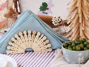 A semicircular napkin holder crafted from wooden pegs holding a pale blue folded napkin on a table setting.