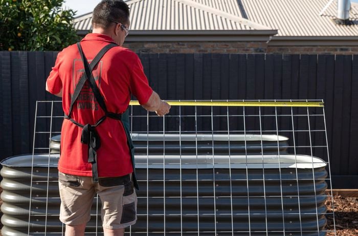 A Bunnings Team Member holding a measuring tape against a piece of wire mesh